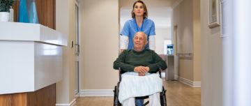 Aide-soignante qui aide un patient dans son fauteuil roulant